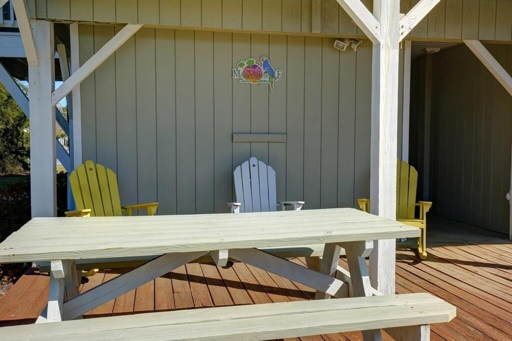 A wooden deck with a picnic table and two Adirondack chairs.