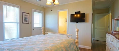 A bedroom with a bed, a ceiling fan, a television mounted on the wall, and a dresser.