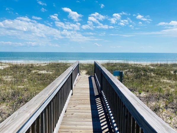 A wooden boardwalk leading to a beach with a clear sky.
