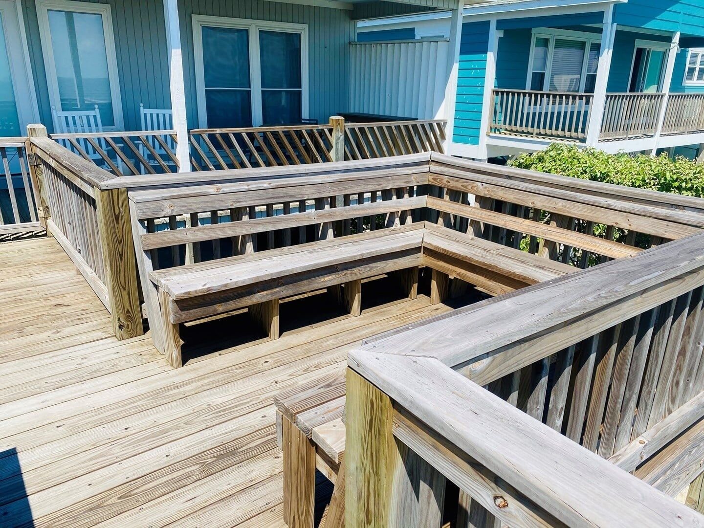 A wooden deck with a built-in bench area, a railing, and a view of a house with a blue exterior.