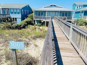 A wooden boardwalk leading to a beachfront property with a sign reading '1005 King of the Sea.'