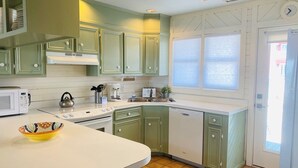 A kitchen with green cabinets, a white countertop, a microwave, a kettle, and a dishwasher.