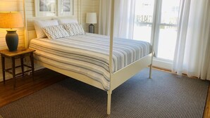 A room with a bed, a nightstand, a lamp, a window with curtains, and a view outside.