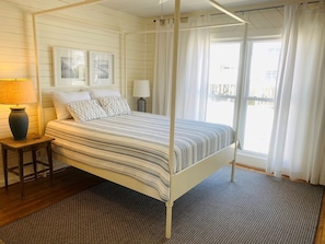 Una habitación con cama, mesita de noche, lámpara, ventana con cortinas y vistas al exterior.