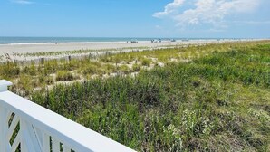 Une plage avec une clôture en bois, des dunes herbeuses et l’océan en arrière-plan.