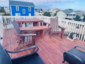 Une terrasse en bois avec une table et des chaises, une maison bleue en arrière-plan et une clôture blanche.