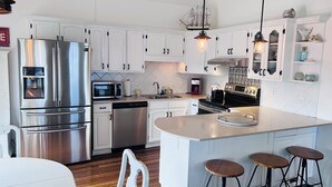 Une cuisine moderne dotée d’appareils électroménagers en acier inoxydable, de meubles blancs et d’un îlot central avec des tabourets.