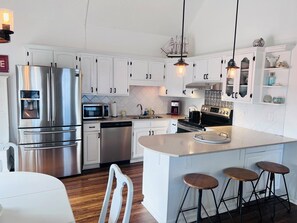 A modern kitchen with stainless steel appliances, white cabinetry, and a central island with stools. - Holden Time 3 Br home by RedAwning (Supply)