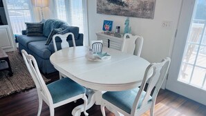 Un coin repas avec une table ronde blanche, quatre chaises blanches, un canapé bleu et un tableau accroché au-dessus de la table.