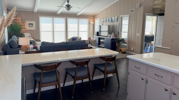 Una cocina moderna con una isla central, taburetes de bar, un ventilador de techo y vistas al área de estar.