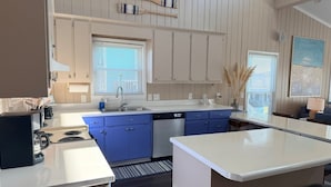 Una cocina moderna con armarios blancos, detalles azules, una isla central y un comedor con taburetes.