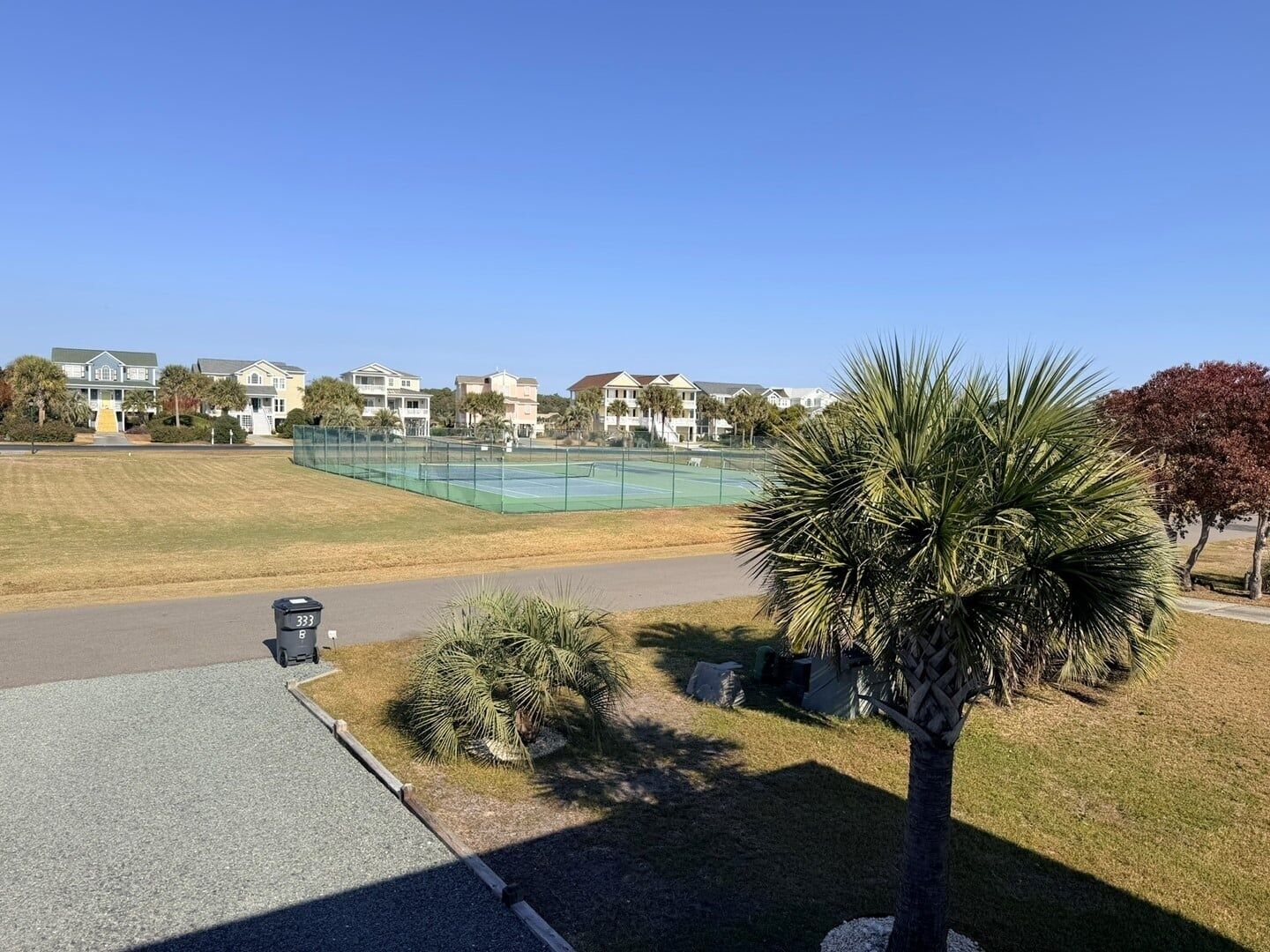 A residential area with a tennis court, houses, and a palm tree.