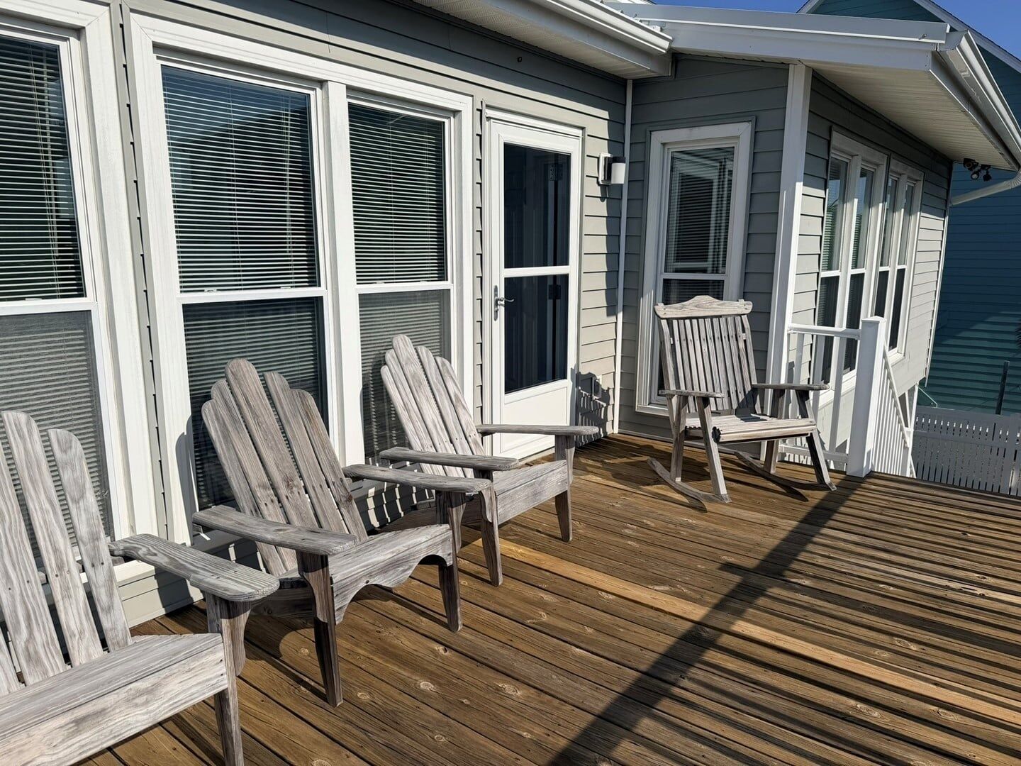 A wooden deck with Adirondack chairs and a house with white siding and multiple windows.