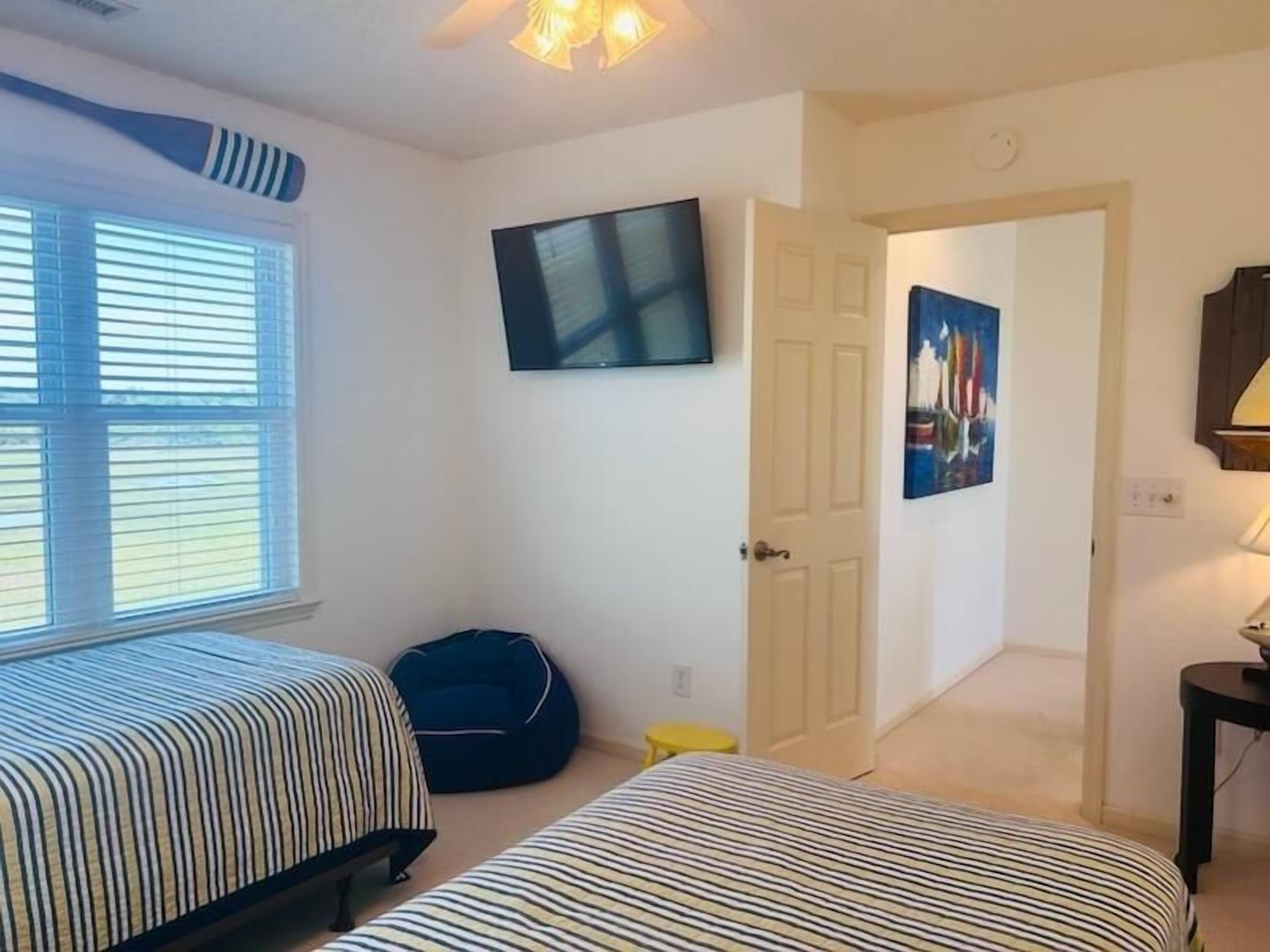 A bedroom with two beds, a TV, a painting, and a door leading to another room.
