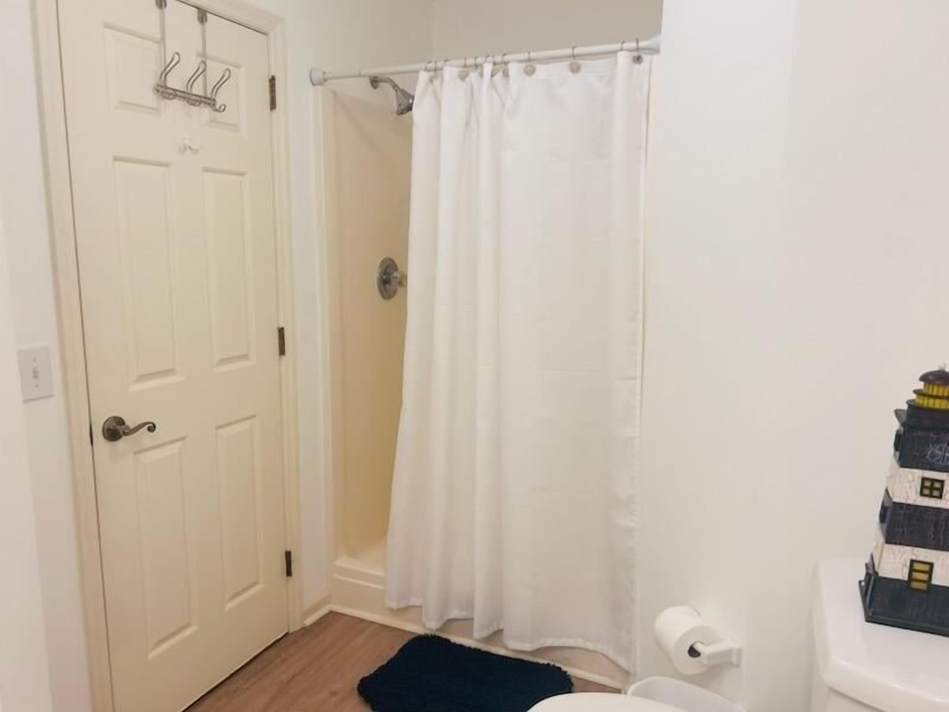 A bathroom with a white door, a shower curtain, a toilet, and a small rug.