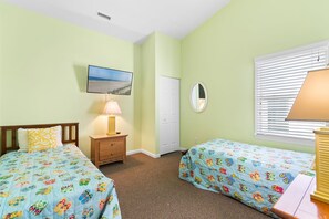 A bedroom with two beds, a nightstand, a lamp, a television, a door, and a window with blinds. - Majak Moments 7 Bedroom Home by RedAwning (Supply)