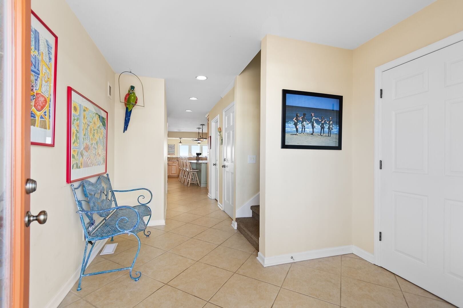 A hallway with a blue metal bench, a framed painting of a parrot, and a framed photograph of people on a beach.