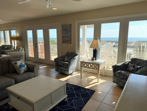 Een ruime woonkamer met uitzicht op het strand, ingericht met een bank, stoelen en een salontafel.