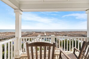 A wooden deck with a white railing, overlooking a beach and ocean.