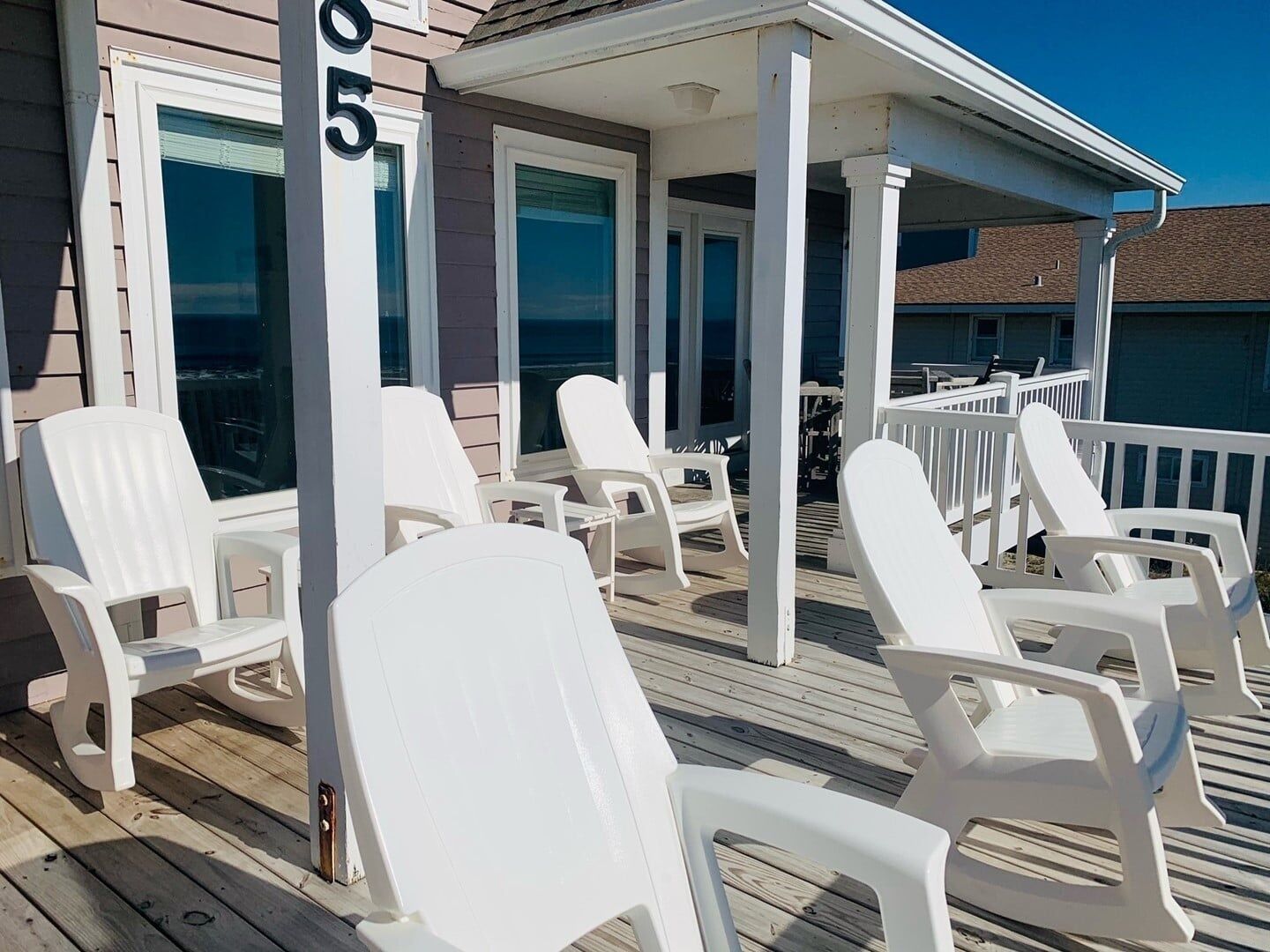 A wooden deck with white plastic chairs and a covered area with a railing.