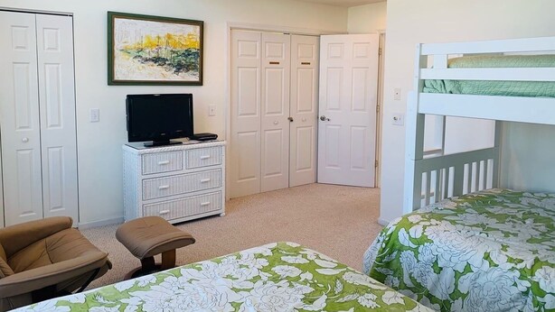 A bedroom with a bunk bed, a television on a dresser, a chair, and a door with a painting. - License To Chill 4 Bedroom Home by RedAwning (Supply)