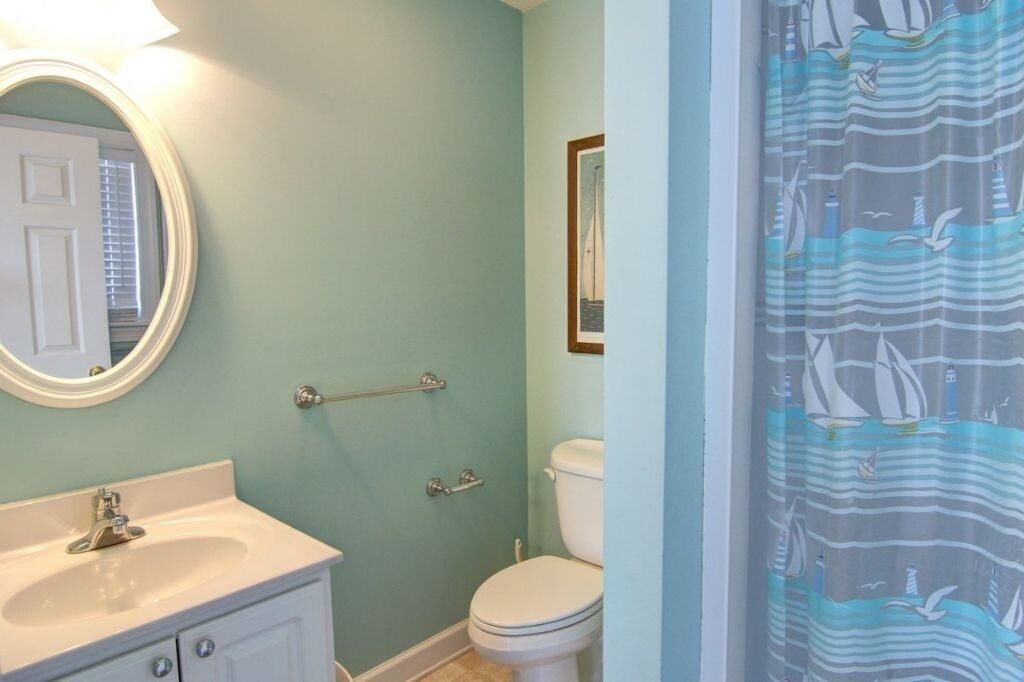 A bathroom with a sink, mirror, toilet, and a shower curtain with a nautical theme.