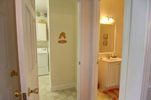 A hallway with a laundry room, a door with a brass handle, and a bathroom with a sink and mirror. - Mclaurin Manna At Holden Beach 4 Bedroom Home by RedAwning (Supply)