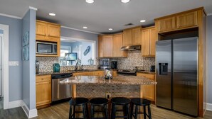 A modern kitchen with wooden cabinets, a stainless steel refrigerator, a microwave, and a tiled backsplash. - Ohana - 4 Br Home (Supply)