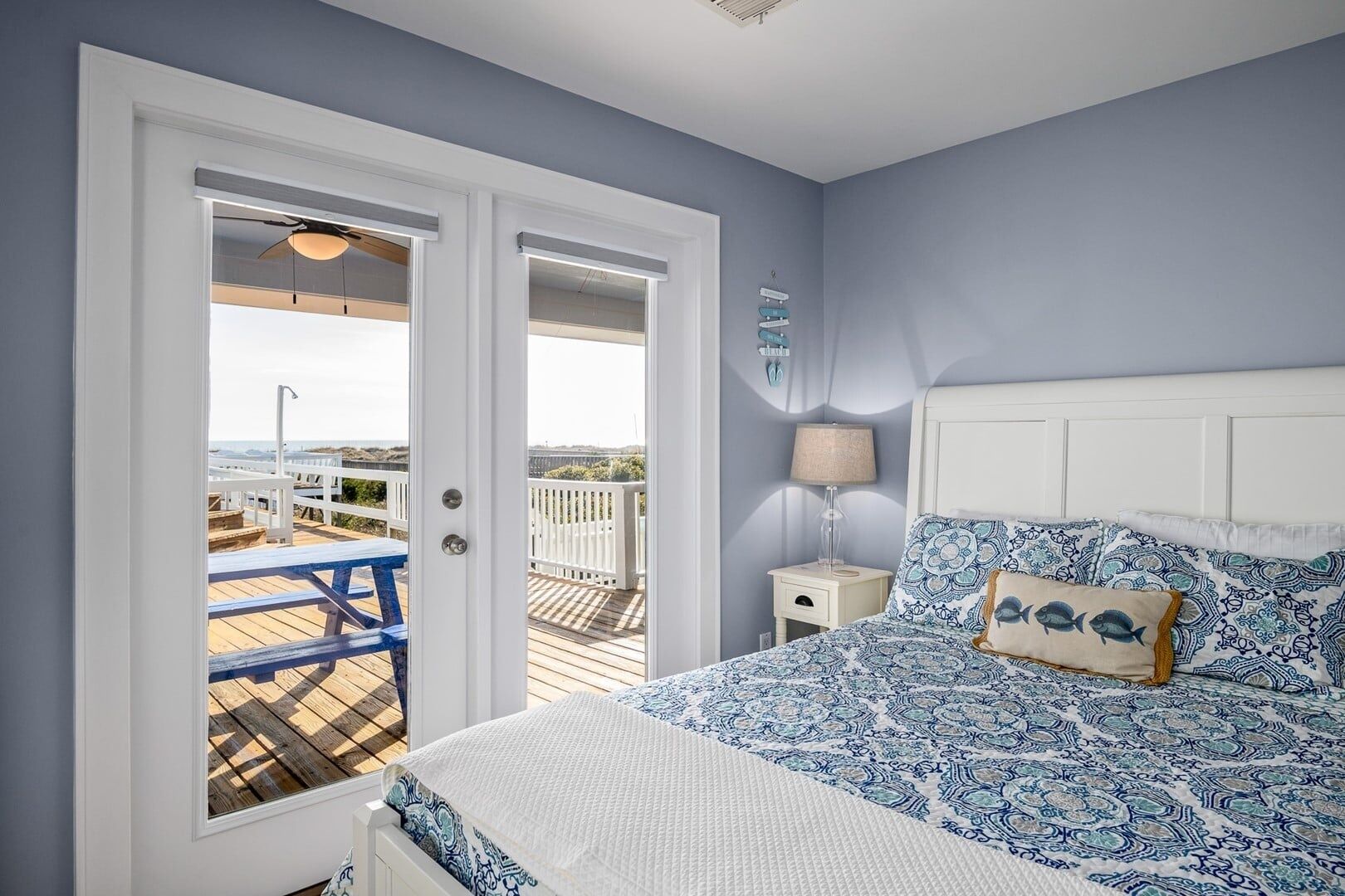 A bedroom with a bed, a nightstand, a lamp, and a view of the deck.