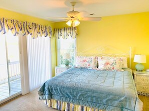 A bedroom with a bed, a ceiling fan, a window with curtains, and a nightstand with a lamp.