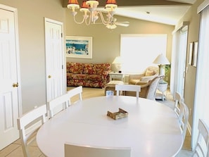 A dining area with a round table, white chairs, a chandelier, and a floral sofa in the background. - Old Man & The Sea 5 Bedroom Home by RedAwning (Supply)