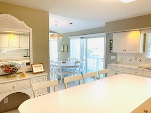 A spacious kitchen with white cabinetry, a large island, and a dining area with white chairs.