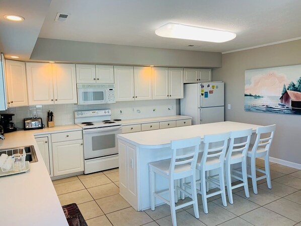 A kitchen with white cabinets, a microwave, a stove, a refrigerator, and a dining area with white chairs.
