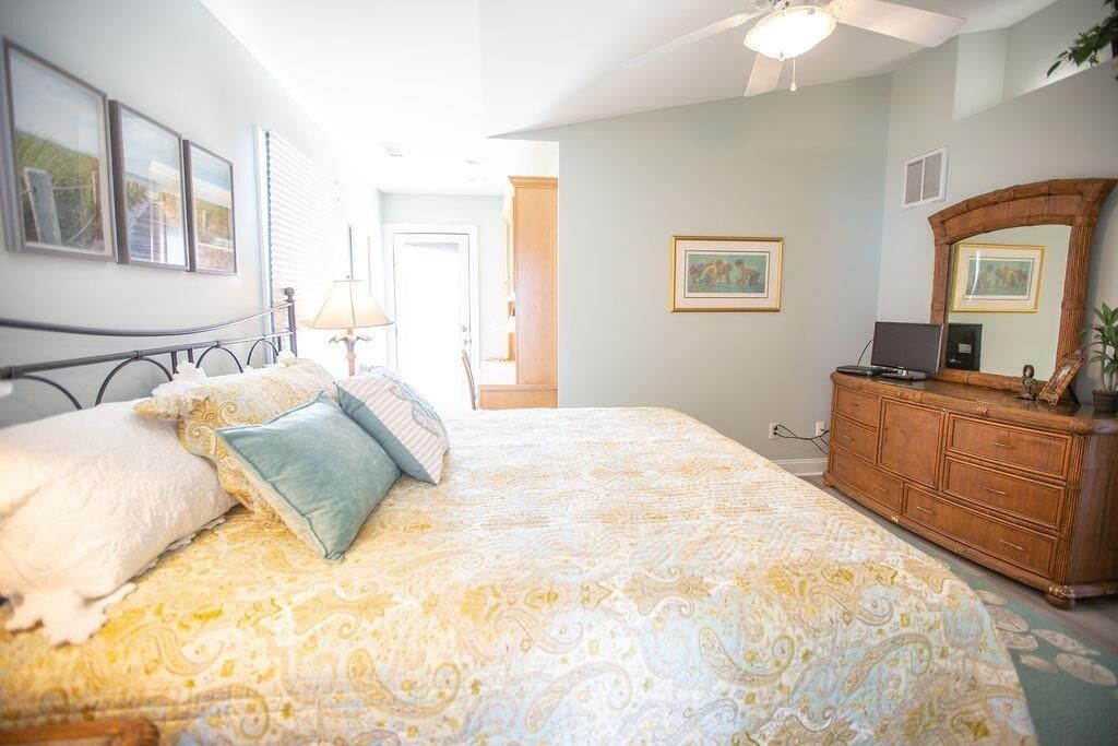 Een slaapkamer met een groot bed, een houten dressoir en een plafondventilator.
