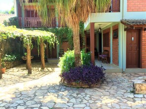 A courtyard with stone flooring, a covered seating area, and a brick building with a wooden door.