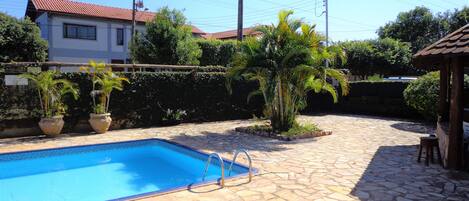 A swimming pool with stone tiles, surrounded by potted plants and a small wooden structure.