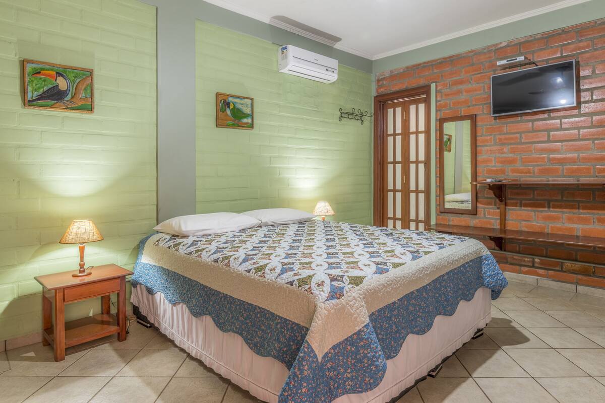A bedroom with a bed, a nightstand, a wall-mounted TV, and a brick wall.