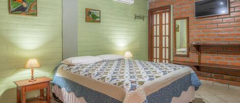 Un dormitorio con cama, mesita de noche, televisor montado en la pared y pared de ladrillo.