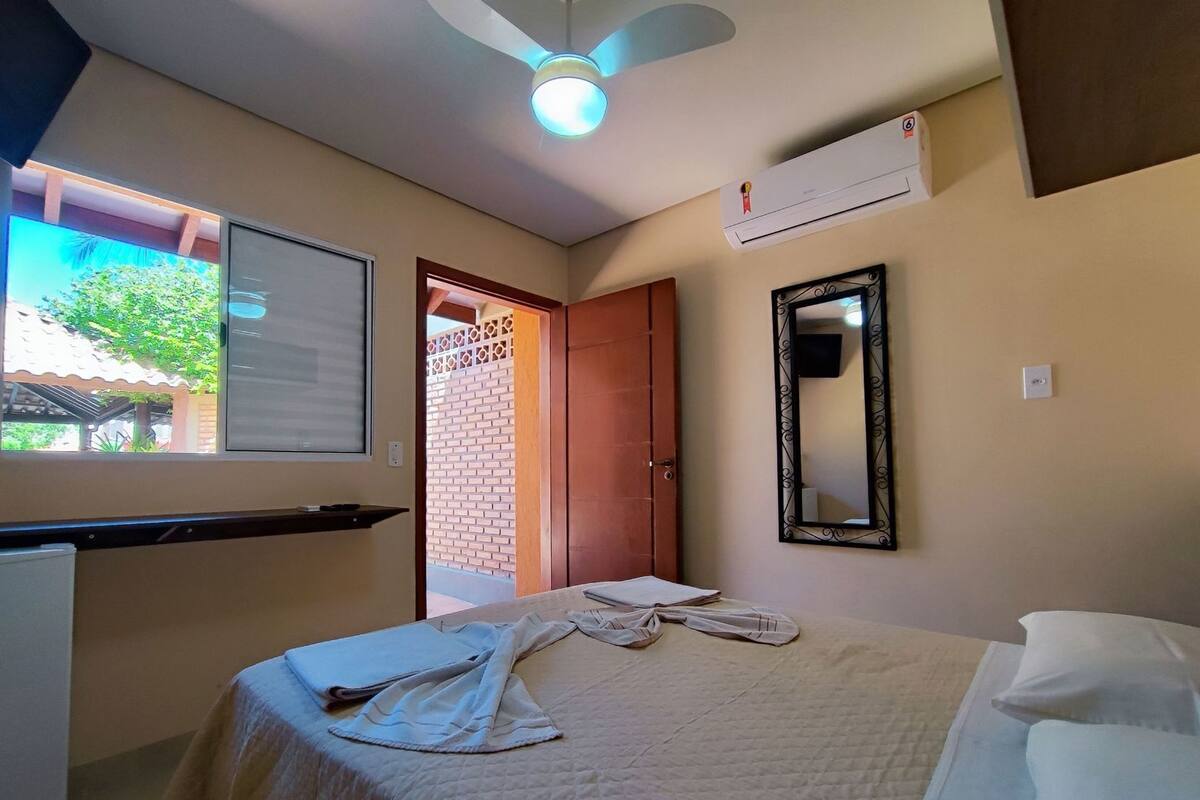 A bedroom with a bed, a desk, a mirror, and an air conditioning unit.