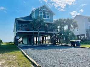 A two-story building with a balcony, a covered area, and a gravel driveway. - Raising The Bar 5 Bedroom Home by RedAwning (Supply)