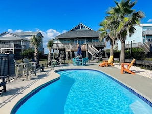 A swimming pool with lounge chairs, a covered deck, and a two-story building with balconies. - Raising The Bar 5 Bedroom Home by RedAwning (Supply)
