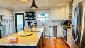 A modern kitchen with a central island, stainless steel appliances, and a wooden floor. - Raising The Bar 5 Bedroom Home by RedAwning (Supply)