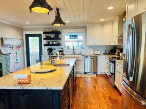 A modern kitchen with a central island, stainless steel appliances, and a wooden floor. - Raising The Bar 5 Bedroom Home by RedAwning (Supply)