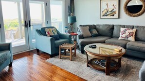 A living room with a sofa, armchair, coffee table, and a view through glass doors. - Raising The Bar 5 Bedroom Home by RedAwning (Supply)