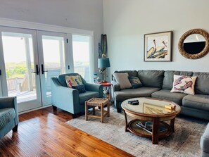 A living room with a sofa, armchair, coffee table, and a view through glass doors. - Raising The Bar 5 Bedroom Home by RedAwning (Supply)