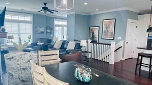 A spacious living room with a dark wooden dining table, a blue patterned armchair, and a ceiling fan.
