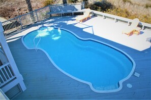 Une piscine dotée d’une terrasse en bois, entourée d’une clôture et aménagée avec des chaises longues.