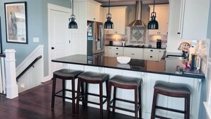 A modern kitchen with a central island, bar stools, pendant lighting, and stainless steel appliances.
