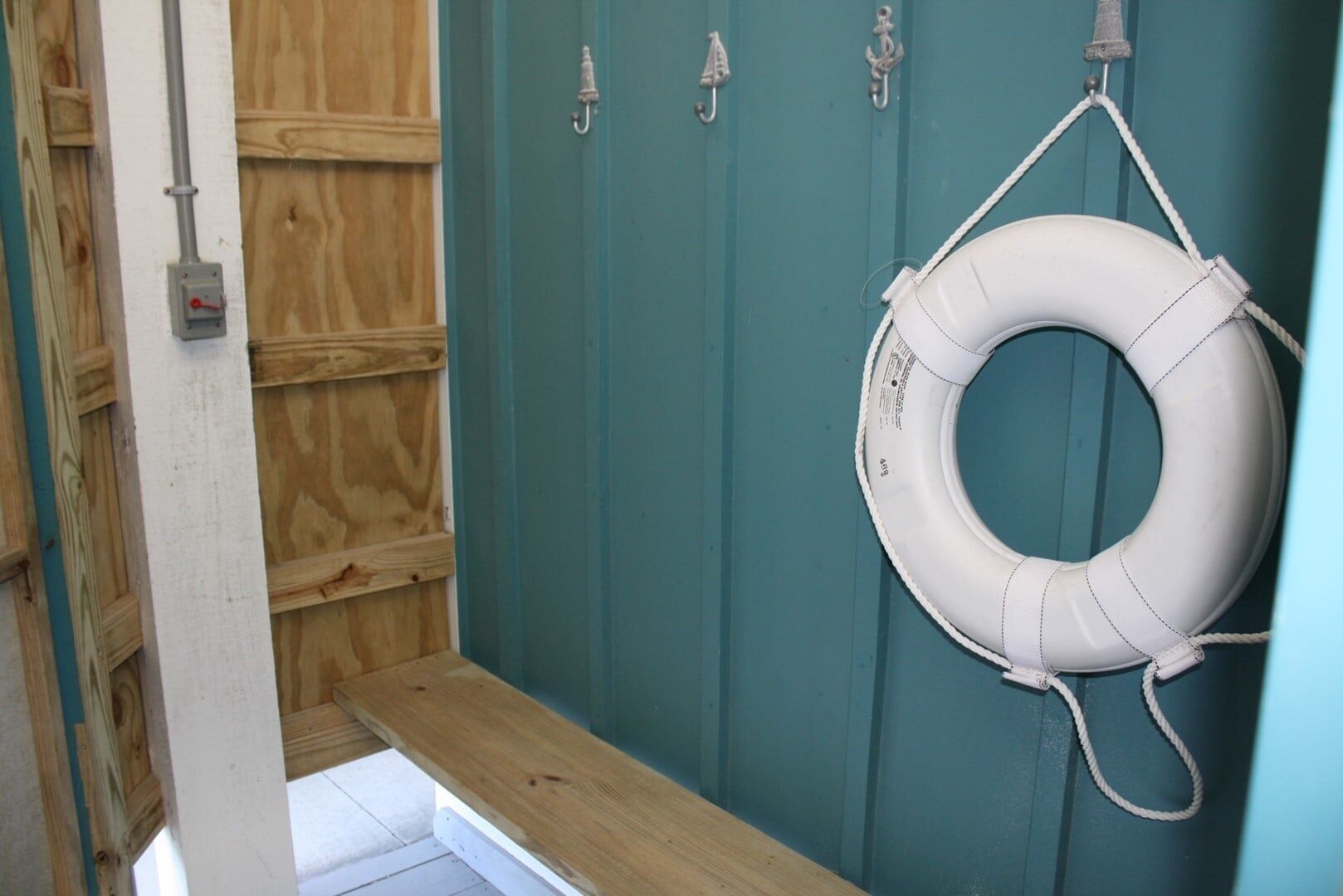 A bathroom with a wooden bench, a teal wall, and a white lifebuoy hanging on hooks.