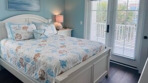 A bedroom with a bed, nightstand, lamp, and a view of the outdoors through a door.